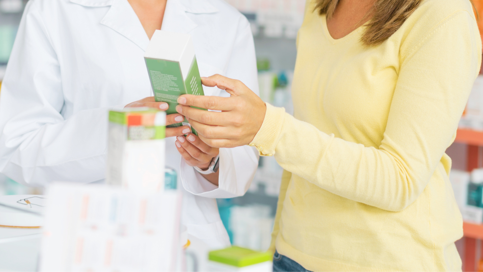 Mani che esaminano la confezione di un prodotto al banco della farmacia