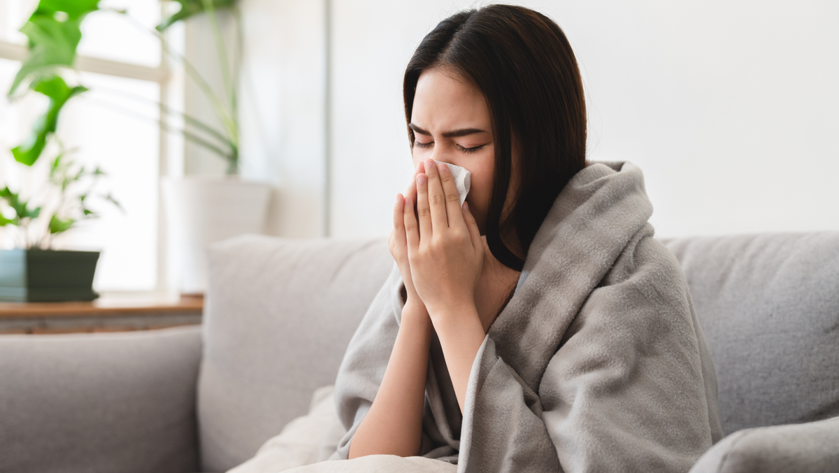 Ragazza con i sintomi dell'influenza si soffia il naso avvolta in una coperta sul divano